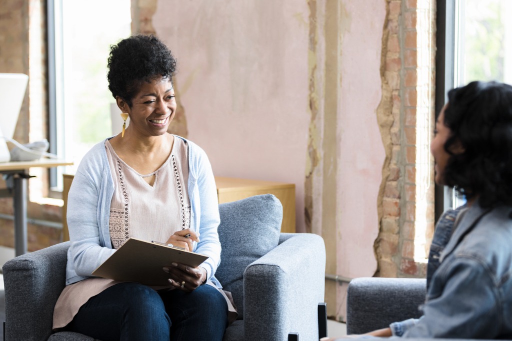 Female therapist and unrecognizable female client smile at each other 