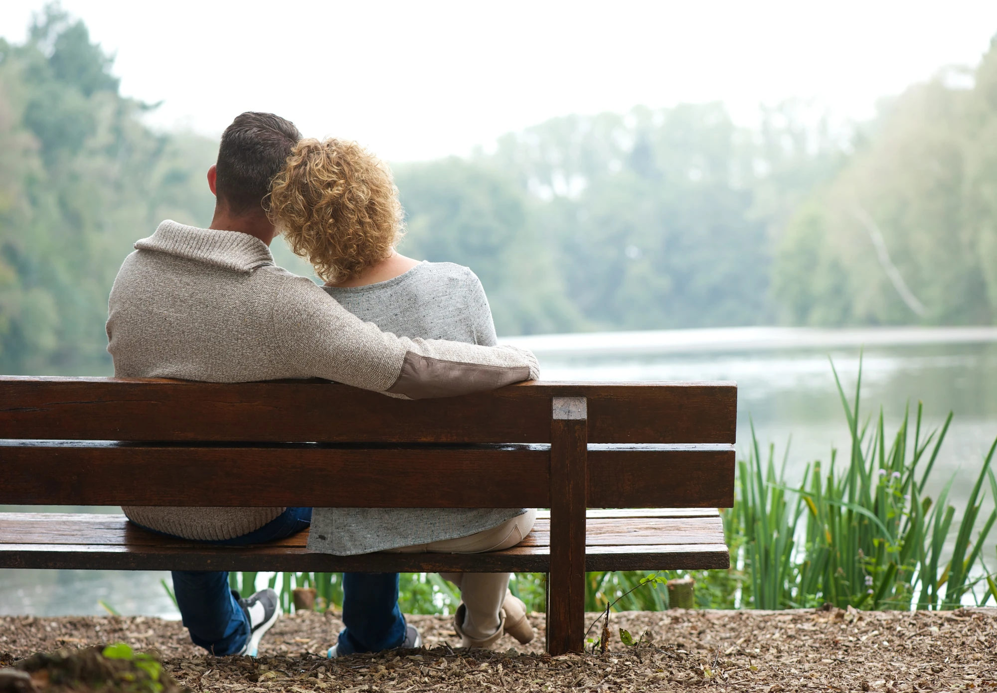 Two adults sitting side by side on a bench outdoors, holding hands and looking calm