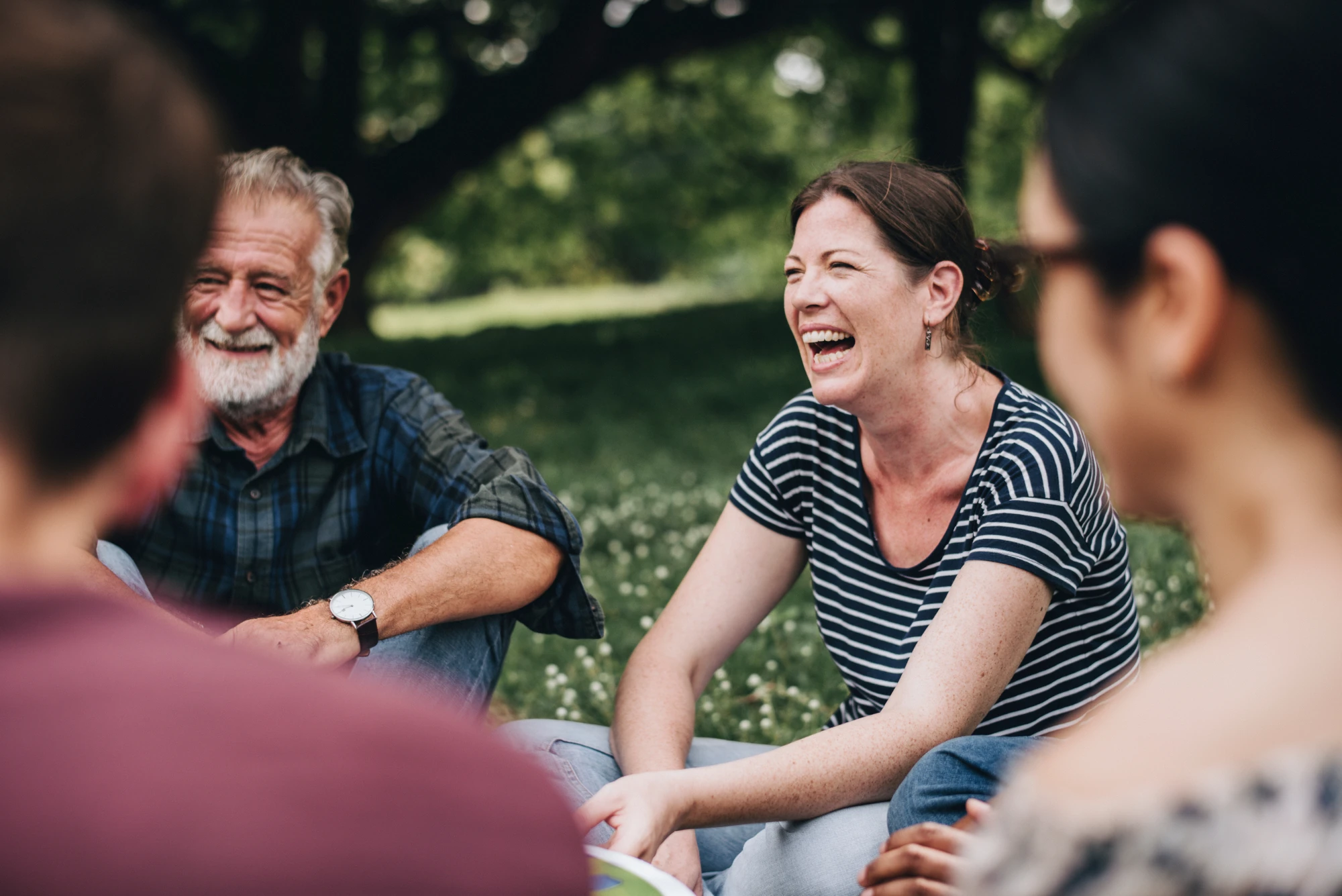 A small group of friends sitting on the grass in a park, talking and smiling together