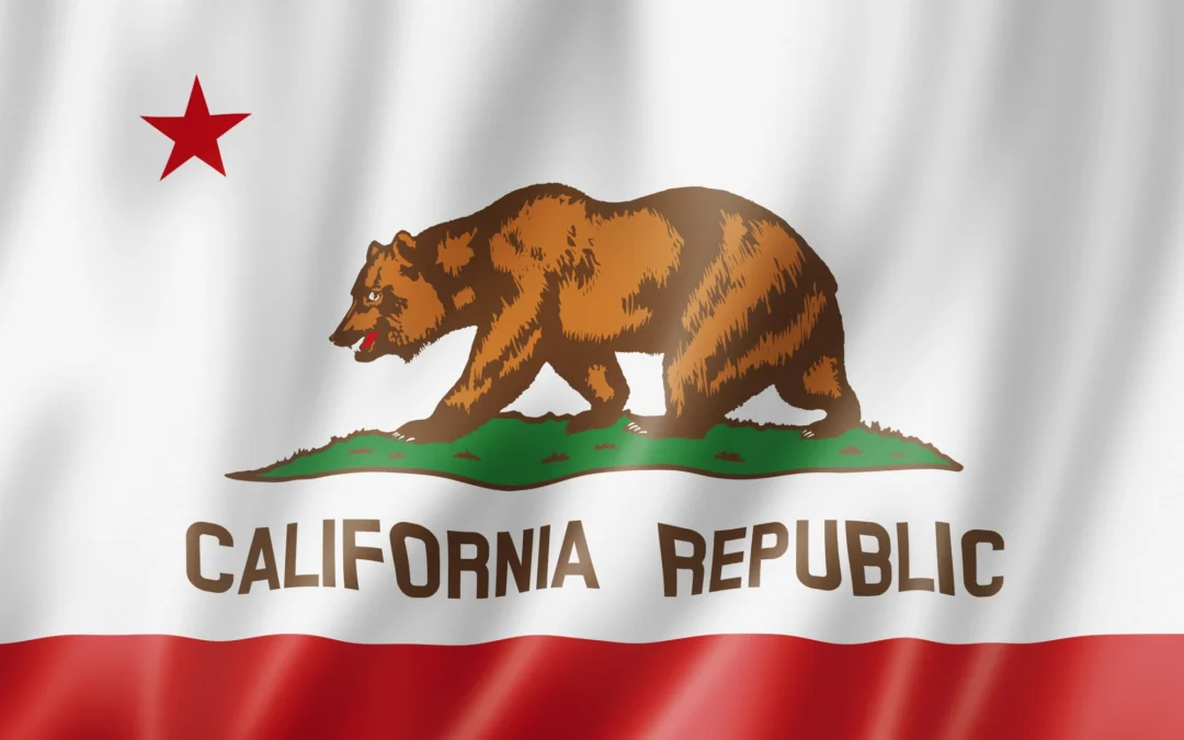 The California state flag with the grizzly bear and star waving against a blue sky