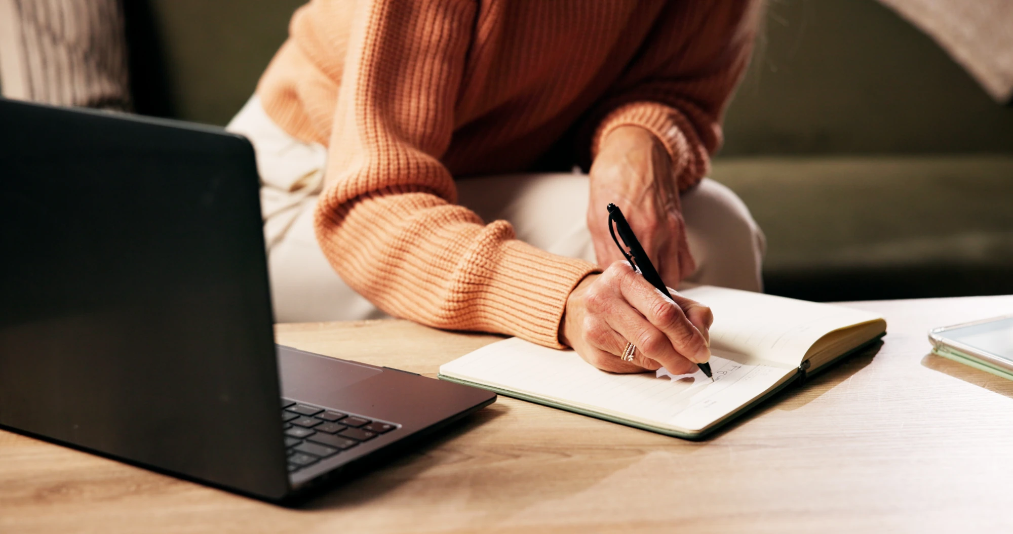 A woman sitting on a couch writing in a notebook, with soft daylight coming through a window