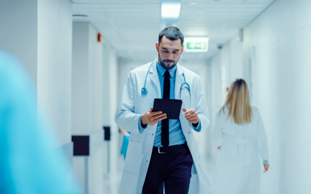 A doctor in a white coat with a stethoscope standing in a quiet hospital hallway, looking down in thought